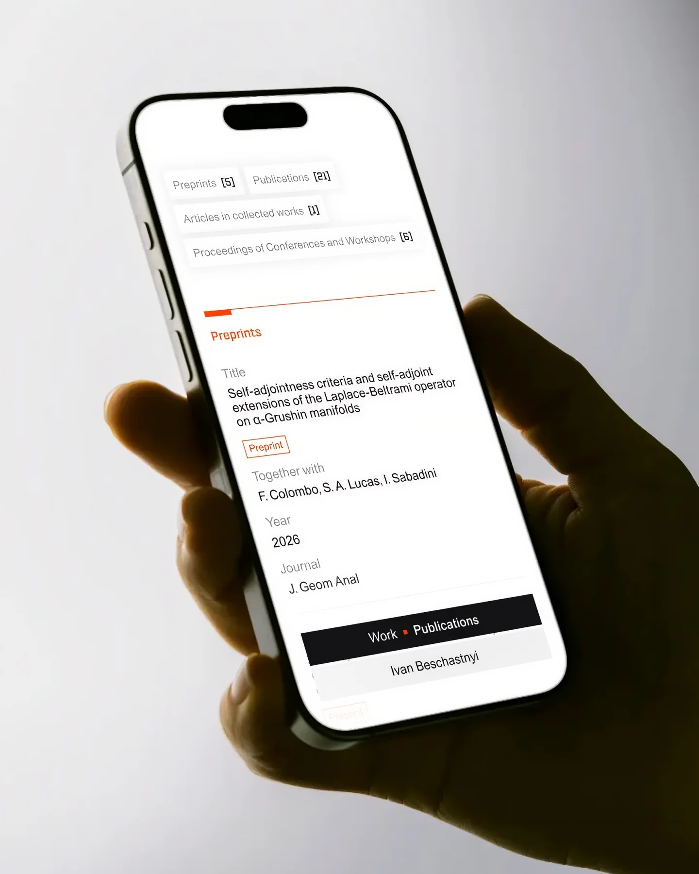 A hand holding a phone displaying Ivan Beschastnyi’s academic website.